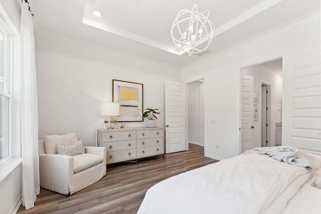 bedroom featuring a notable chandelier, wood finished floors, baseboards, ornamental molding, and a tray ceiling