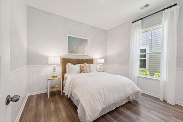 bedroom with wainscoting, wood finished floors, visible vents, and baseboards