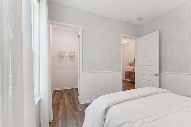 bedroom with a closet, wainscoting, wood finished floors, and a walk in closet