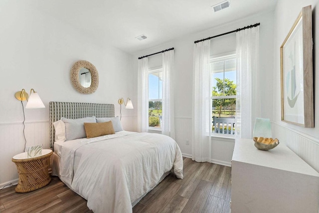 bedroom with wainscoting, wood finished floors, and visible vents