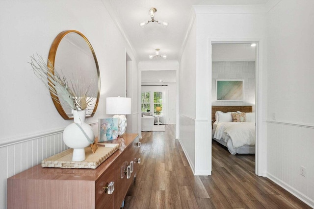 corridor with a wainscoted wall, ornamental molding, and dark wood-style flooring