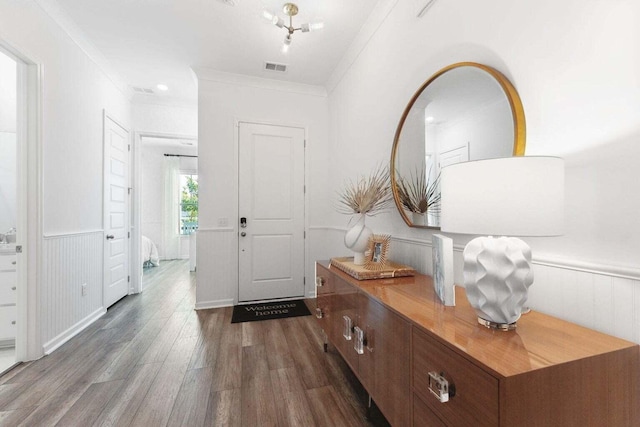 foyer entrance with a wainscoted wall, crown molding, visible vents, and dark wood-type flooring