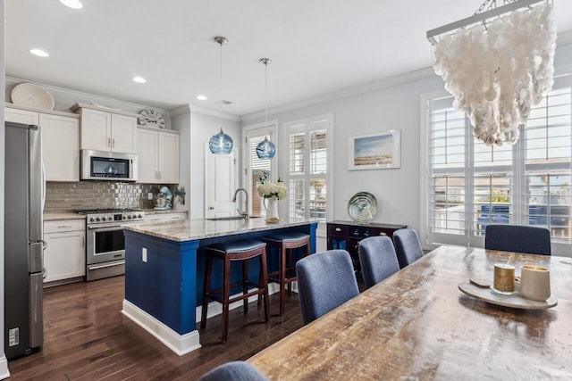 kitchen featuring a breakfast bar, a sink, white cabinetry, appliances with stainless steel finishes, and tasteful backsplash