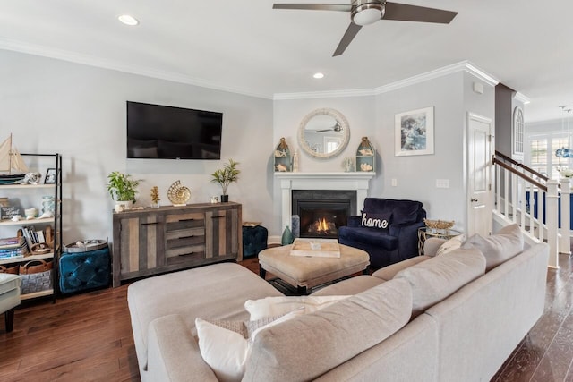 living room with a warm lit fireplace, ornamental molding, stairway, and wood finished floors