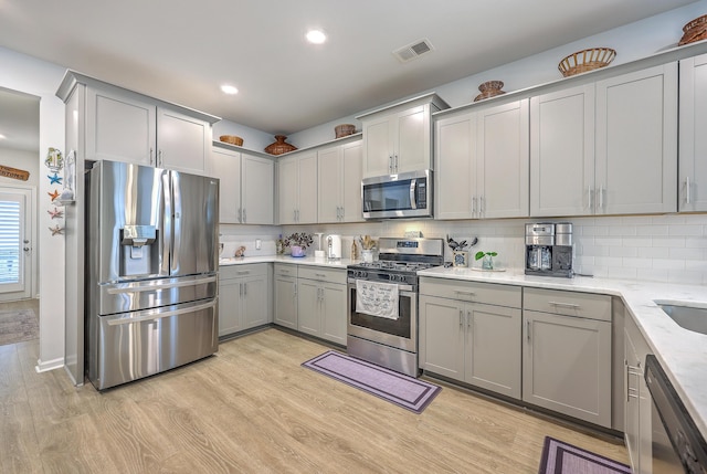 kitchen with visible vents, gray cabinets, stainless steel appliances, light wood finished floors, and backsplash
