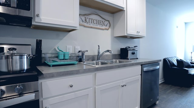 kitchen with appliances with stainless steel finishes, a sink, white cabinetry, and wood finished floors