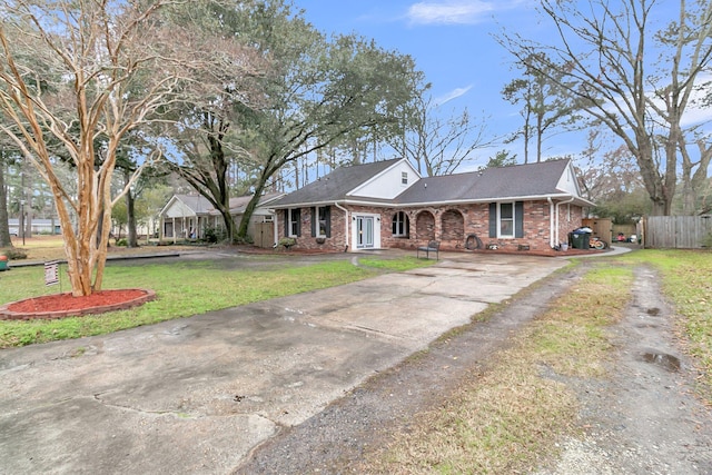 ranch-style house with driveway, brick siding, fence, and a front yard