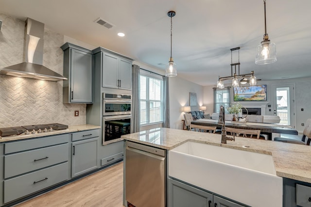 kitchen with decorative light fixtures, visible vents, appliances with stainless steel finishes, open floor plan, and wall chimney range hood