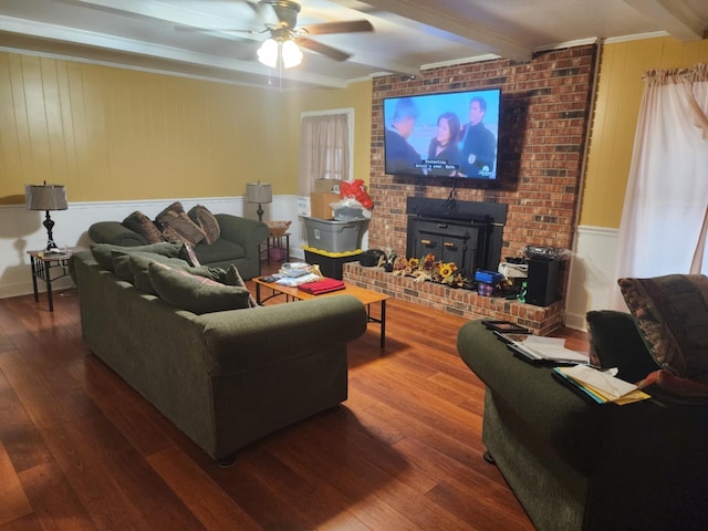 living room with hardwood / wood-style floors, a wood stove, ceiling fan, ornamental molding, and beam ceiling