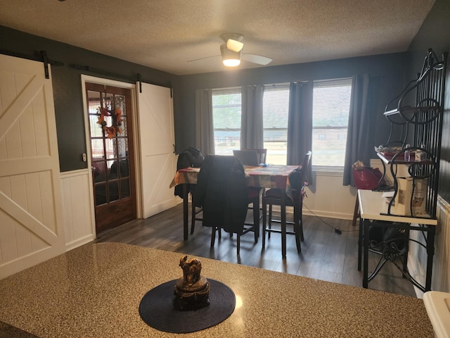 dining area with a textured ceiling, a barn door, ceiling fan, and dark wood-type flooring