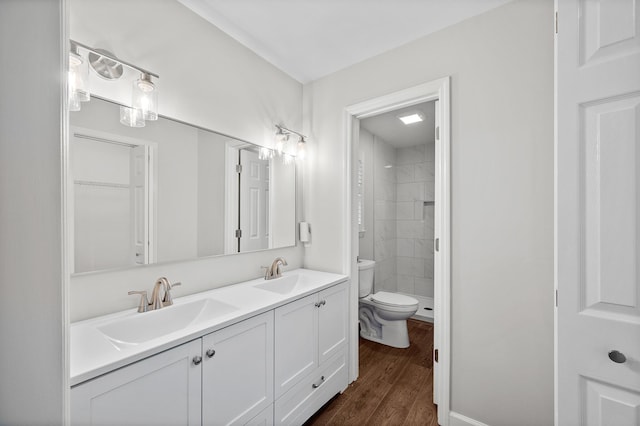 bathroom with hardwood / wood-style flooring, vanity, a tile shower, and toilet