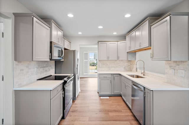 kitchen with sink, gray cabinetry, appliances with stainless steel finishes, light hardwood / wood-style floors, and backsplash