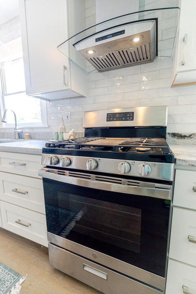 2020 Piper Dr, Charleston, SC 29407 - kitchen with gas stove, ventilation hood, white cabinetry, light stone counters, and decorative backsplash