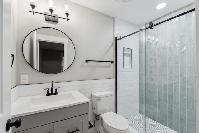 bathroom with a shower with door, vanity, tile walls, and toilet