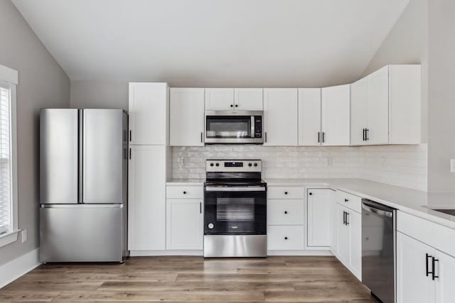 kitchen featuring lofted ceiling, light hardwood / wood-style flooring, white cabinetry, stainless steel appliances, and decorative backsplash