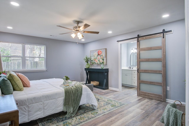 bedroom with recessed lighting, light wood-style flooring, baseboards, and a barn door