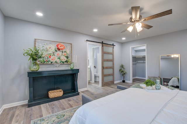 bedroom featuring a barn door, recessed lighting, wood finished floors, baseboards, and ensuite bath