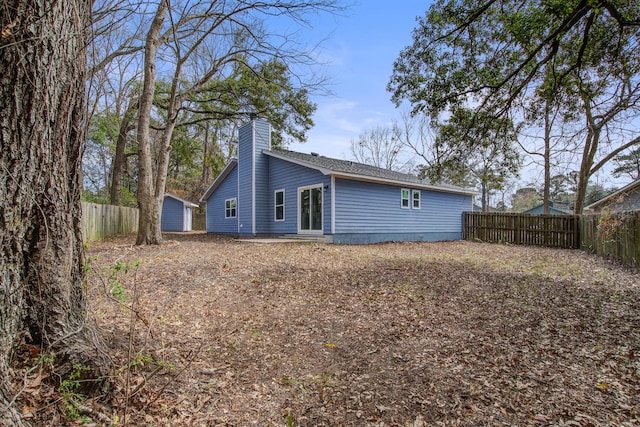 rear view of house with an outbuilding, a fenced backyard, a chimney, and a storage shed