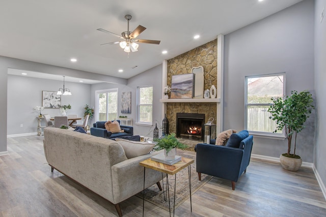 living area featuring light wood-style flooring, baseboards, vaulted ceiling, and a stone fireplace