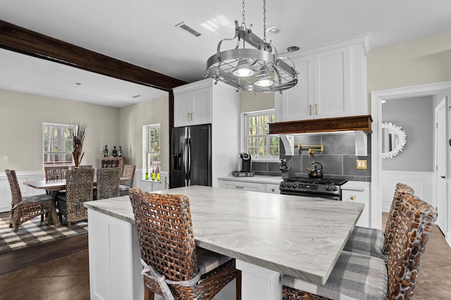 kitchen with beam ceiling, stainless steel appliances, a center island, light stone countertops, and white cabinets