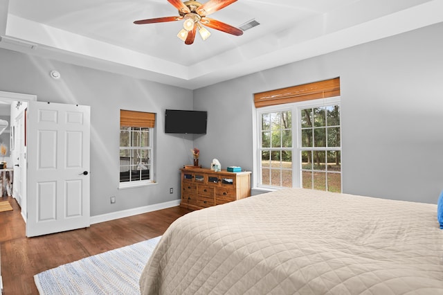 bedroom with a tray ceiling, dark wood-type flooring, and ceiling fan