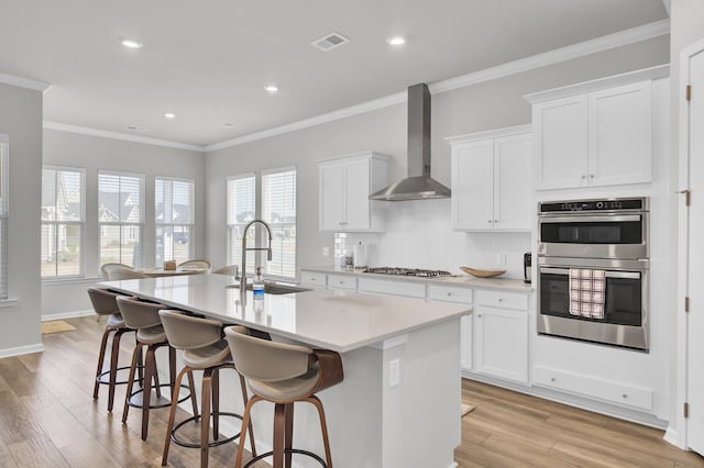 kitchen featuring white cabinets, sink, a kitchen island with sink, and wall chimney exhaust hood