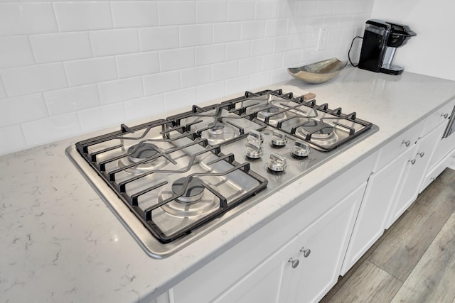 details with gas stovetop, backsplash, wood-type flooring, and white cabinets