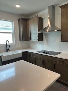 kitchen with black electric stovetop, dark brown cabinetry, dark wood-type flooring, sink, and wall chimney range hood