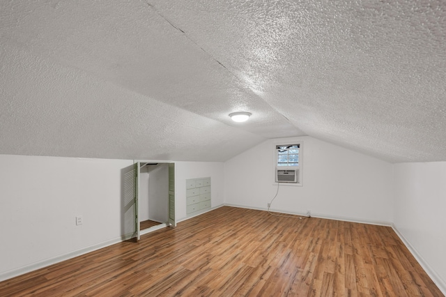 additional living space with a textured ceiling, hardwood / wood-style floors, cooling unit, and vaulted ceiling