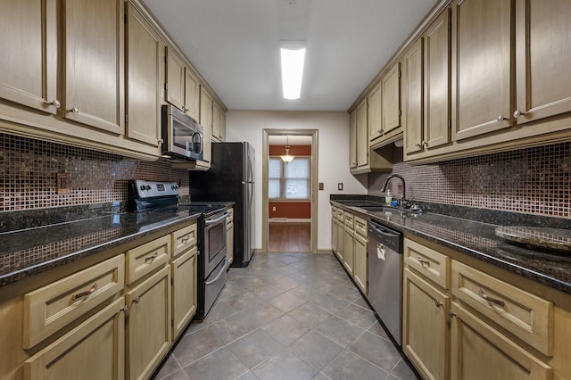 kitchen with sink, stainless steel appliances, tile patterned flooring, dark stone countertops, and decorative light fixtures