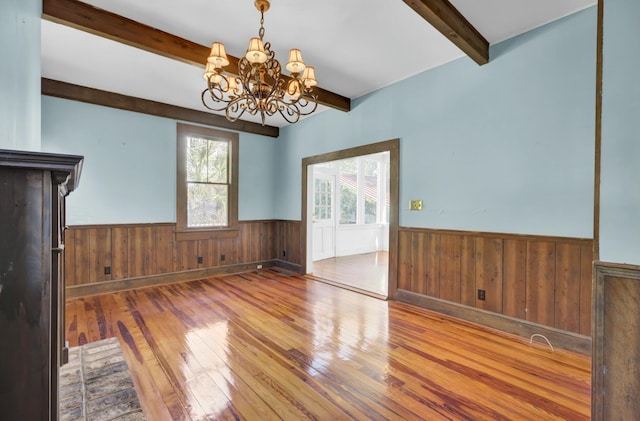 unfurnished dining area featuring hardwood / wood-style flooring, beam ceiling, and an inviting chandelier