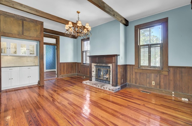 unfurnished living room featuring beam ceiling, plenty of natural light, a fireplace, and wood-type flooring