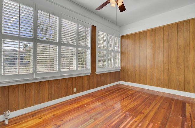 spare room with ceiling fan, wood-type flooring, and wood walls