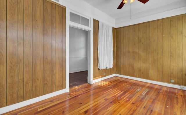 unfurnished bedroom featuring ceiling fan, hardwood / wood-style flooring, and wooden walls