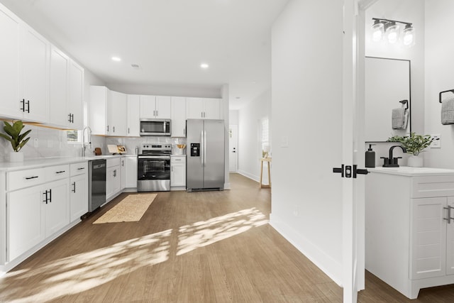 kitchen featuring white cabinets, decorative backsplash, light wood-type flooring, and appliances with stainless steel finishes