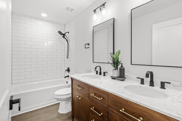 full bathroom featuring vanity, hardwood / wood-style floors, tiled shower / bath combo, and toilet