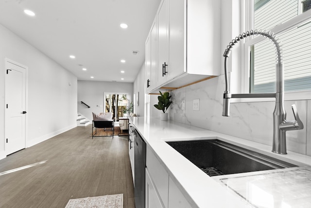 kitchen with dark hardwood / wood-style flooring, backsplash, stainless steel dishwasher, sink, and white cabinets