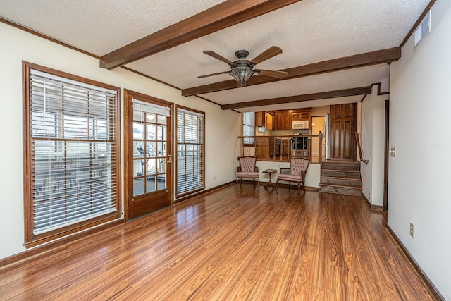 unfurnished living room featuring ceiling fan, beamed ceiling, light hardwood / wood-style floors, and a textured ceiling