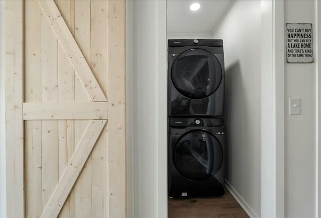 washroom with stacked washer and dryer, wood-type flooring, and a barn door