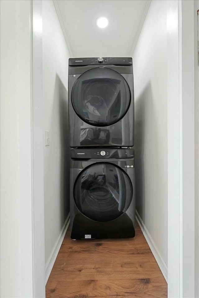 laundry area with stacked washer / drying machine, wood-type flooring, and ornamental molding