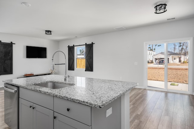 kitchen featuring light stone countertops, stainless steel dishwasher, sink, a barn door, and an island with sink