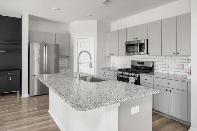 kitchen with appliances with stainless steel finishes, a center island with sink, light stone counters, and sink