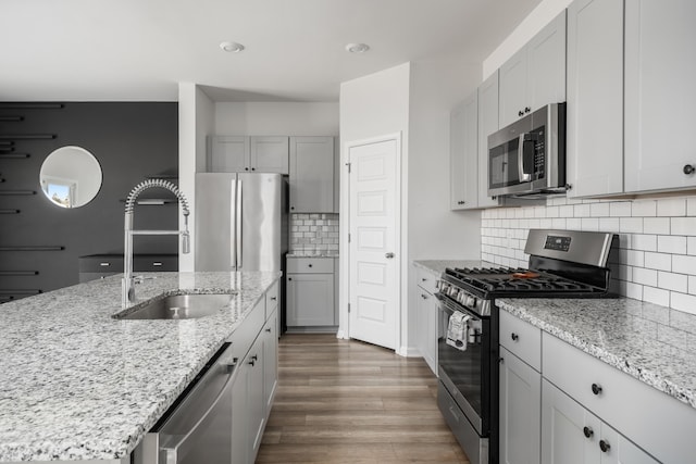 kitchen with light stone countertops, backsplash, stainless steel appliances, sink, and a center island with sink