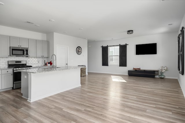 kitchen with sink, stainless steel appliances, backsplash, an island with sink, and gray cabinets