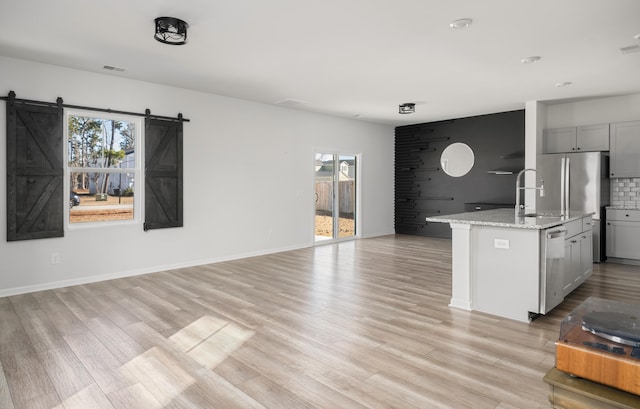 kitchen featuring a barn door, light stone counters, stainless steel dishwasher, an island with sink, and gray cabinets