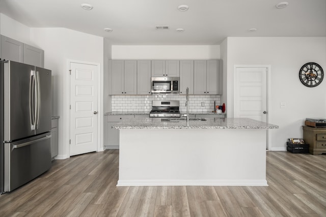 kitchen with backsplash, a kitchen island with sink, sink, light stone counters, and stainless steel appliances