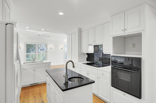 kitchen featuring a kitchen island with sink, ceiling fan, a sink, and black appliances
