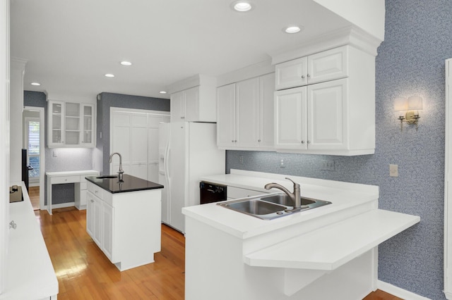 kitchen with a sink, an island with sink, light wood-style floors, a peninsula, and black appliances