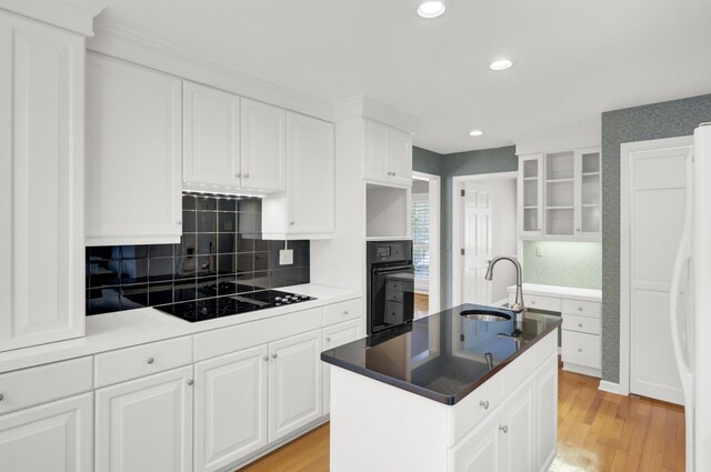 kitchen featuring light wood finished floors, a sink, black appliances, and white cabinetry