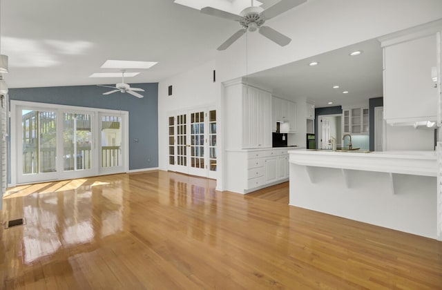 unfurnished living room with vaulted ceiling with skylight, ceiling fan, light wood-style flooring, visible vents, and recessed lighting